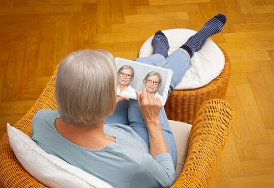 Older woman looks at a laptop displaying images of herself wearing glasses