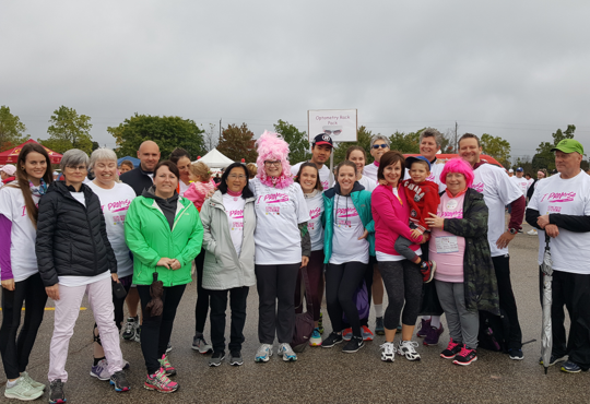A group of smiling people wearing running gear stand in a parking lot under a cloudy sky