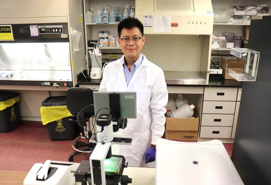 Will Ngo stands behind a microscope in his lab