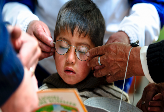 Image of a child holding his father's hand while Optometrists test his vision