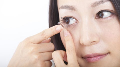 A woman inserts a contact lens into her eye