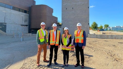 EssilorLuxottica representatives and School staff stand in the contruction area wearing hard hats and reflective vests.