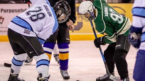 Two hockey players face off as a puck drops to the ice.