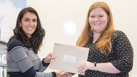Dr. Shamrozé Khan smiles and shakes Jessica Wood’s hand as she passes Jessica an envelope.