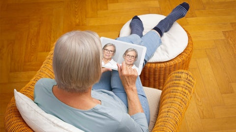 Older woman looks at a laptop displaying images of herself wearing glasses