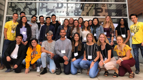 Large group of young people standing in front of glass wall imprinted with eye chart