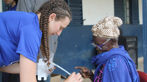 A young woman wearing blue leans over an older woman to show her an eye chart