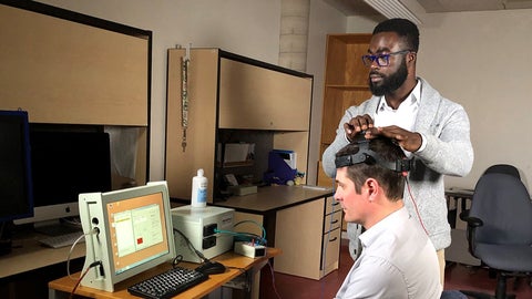 Richard Donkor looks at a computer monitor while adjusting Dr. Ben Thompson’s headset