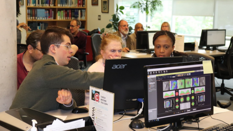 A man points at a computer screen while another man and two women look at the screen