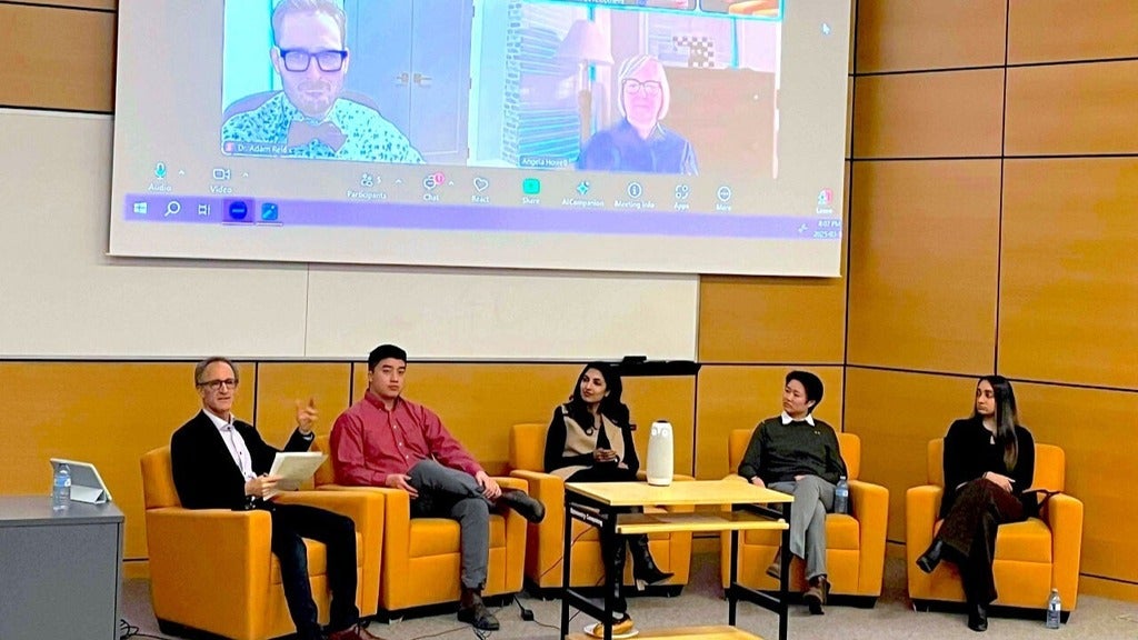 CAOS panel sitting in front of a large screen showing virtual panel members