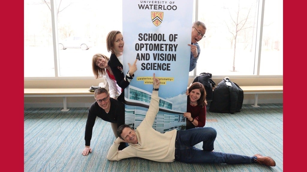 A group of smiling alums pointing to a UWOVS sign