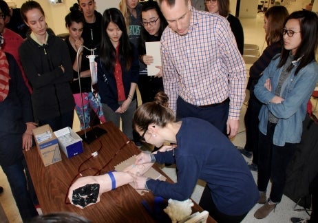 Students practising intravenous injections on a plastic arm