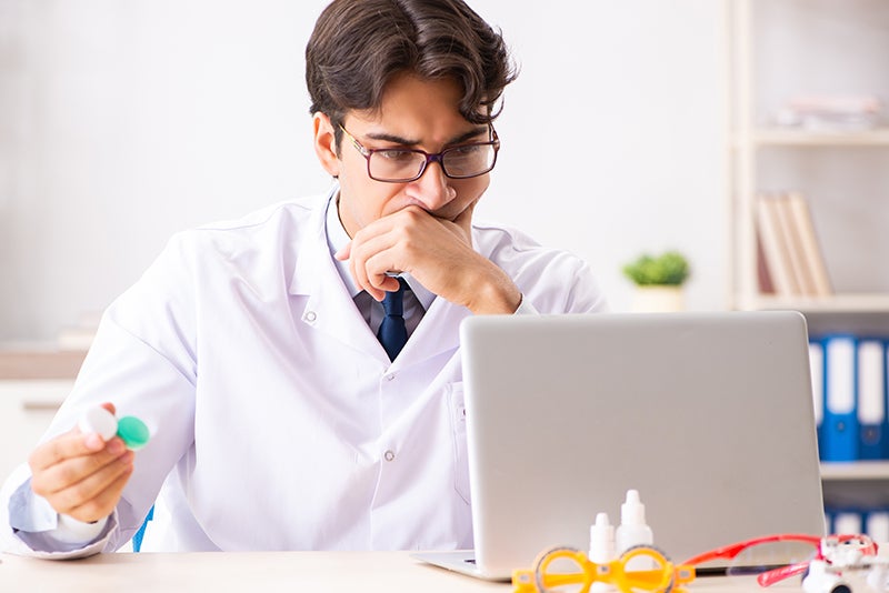 Optometrist holds a contact lens case as he looks at a laptop