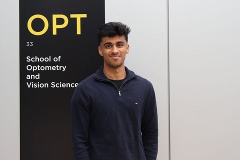 Om Parekh standing outside the University of Waterloo School of Optometry and Vision Science sign.