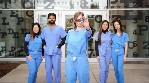 Five students in scrubs, one holding a lens