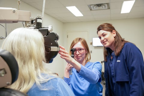 An optometry intern examining a patient under supervision of a clinician.