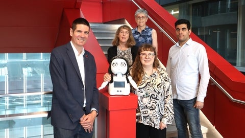 Five people posing with childlike robot