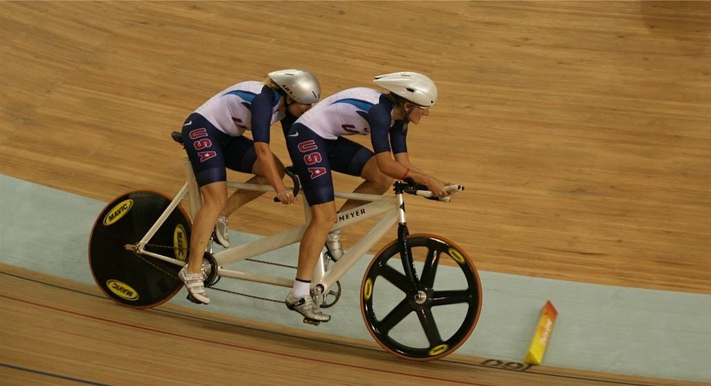 Two cyclists on a tandem bike race on a velodrome track