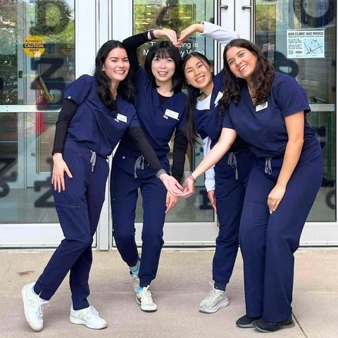 Four young women in scrubs making a heart shape with their arms