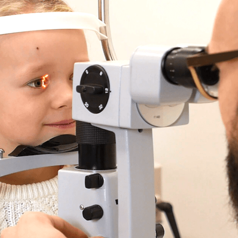 Optometrist looks in eyes of child patient using optometric equipment