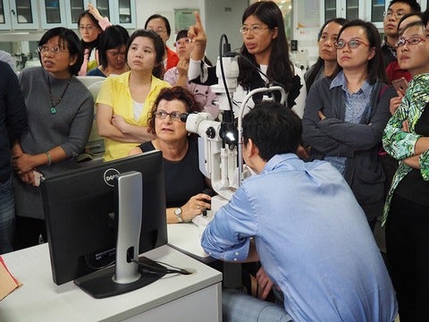 Dr. Gina Sorbara is surrounded by young people as she sits in front of a slit lamp