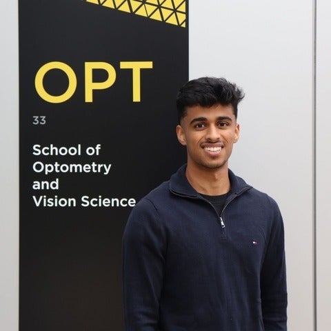 Om Parekh standing outside the University of Waterloo School of Optometry and Vision Science sign.