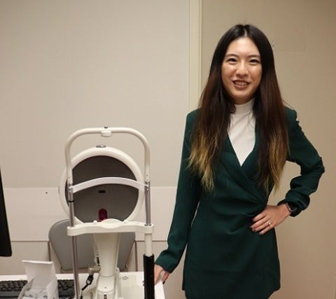 Dr. Sharon Qiu stands beside a table with optometric equipment
