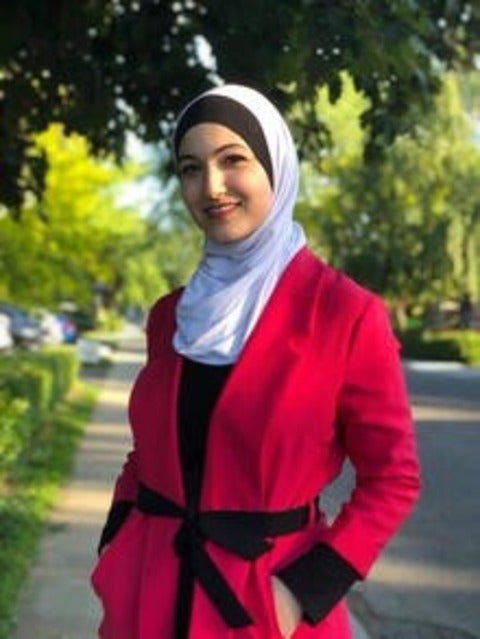 Yara Mohiar, dressed in a white hijab and red coat, stands ona tree-lined street 