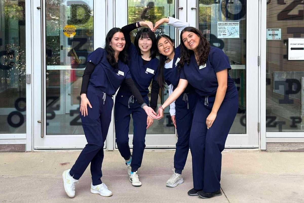 Four young women in scrubs make a heart shape with their arms.