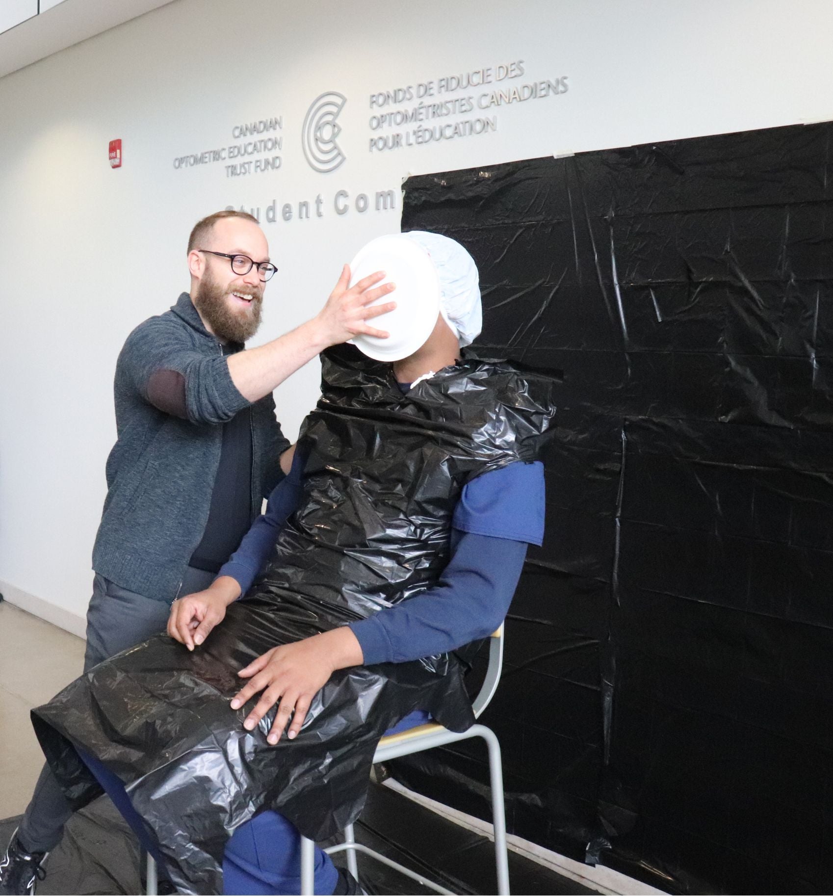 Details in caption. Man throws pie in another student's face.