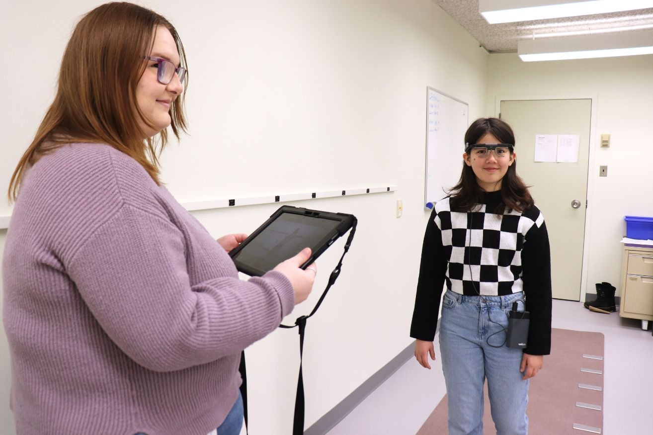 Woman holds ipad while child wearing eye tracking glasses walks