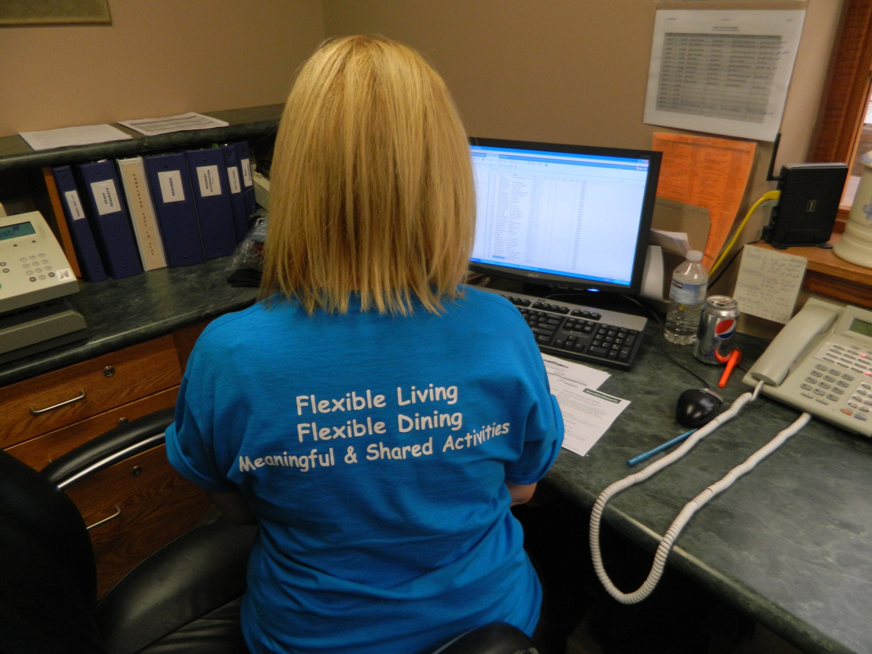 Staffer sits with back to camera wearing t-shirt which reads 'flexible living, flexible dining, meaningful and shared activities'