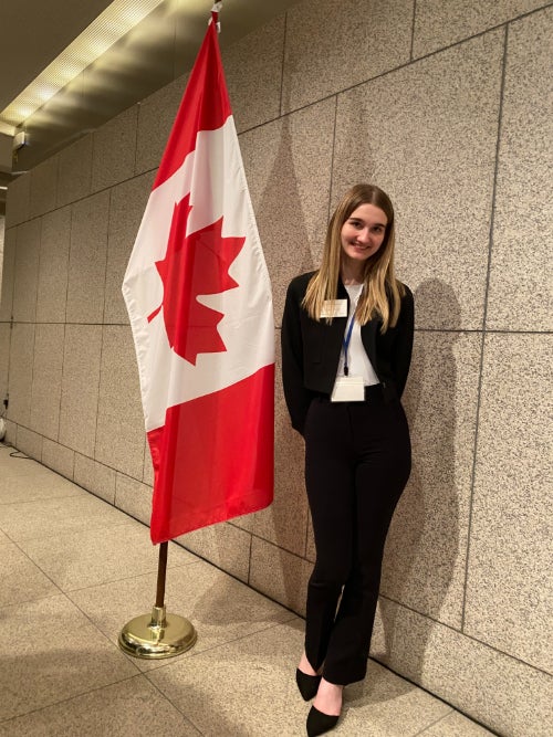 Picture of woman standing beside the Canadian flag at a conference