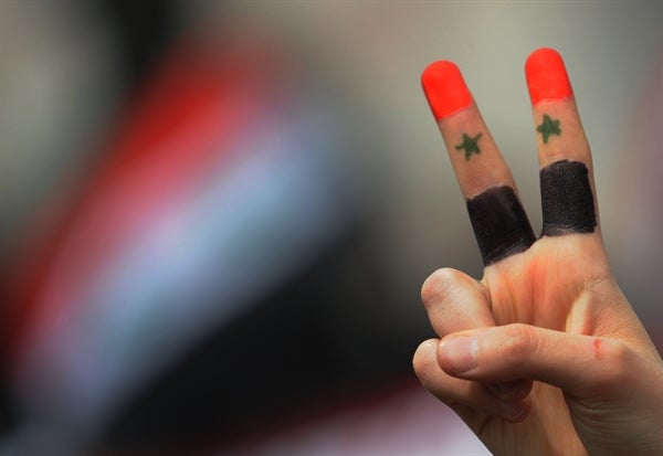Hand in a peace sign painted with the colours of the Syrian flag