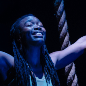 Black actress faces the sky with her eyes closed with an expression somewhere between struggle and victory