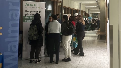 Students standing in a hallway chatting with employers at booths