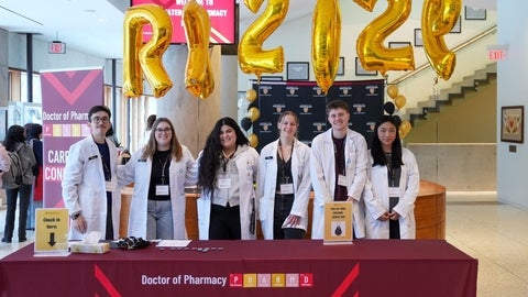 A group of students smiling behind a welcome table
