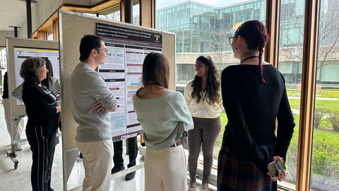 A group of people clustered around a scientific poster listening to a graduate student present