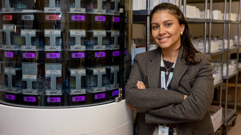 Person standing beside an automated medication dispensing system in a hospital pharmacy.
