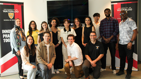 Group of students and faculty posing indoors between University of Waterloo School of Pharmacy banners.
