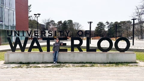 Luca Roy standing in front of the University of Waterloo sign