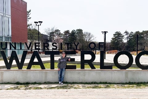 Luca Roy standing in front of the University of Waterloo sign