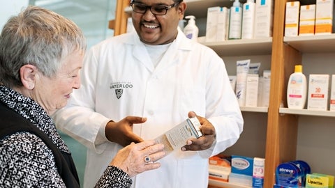 A male pharmacist holding a medicine and talking to an elderly patient.