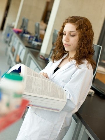 Pharmacy student in white coat reading a textbook