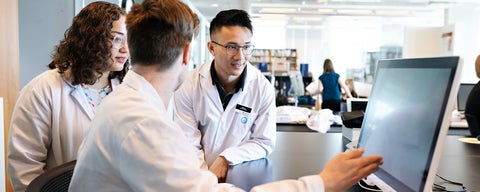 Three students working together in a clinic while looking at a computer screen.