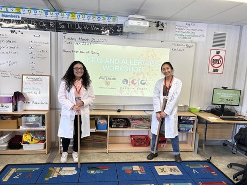 Two pharmacy students standing at the front of an elementary school class.