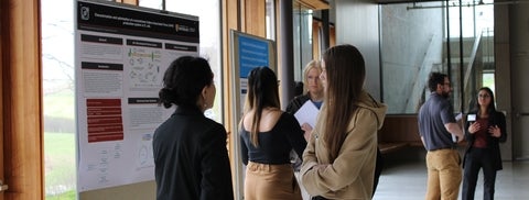 Graduate presenting research baord with others listening and chatting