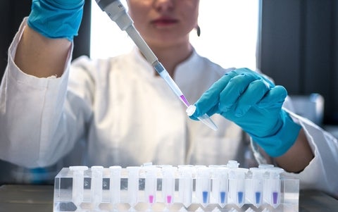 Female scientist pipetting colored chemicals into a tube.