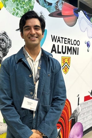 Alumni smiling in front of poster that says 'alumni'