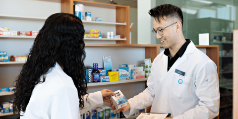 Two students in white coats talking in a pharmacy